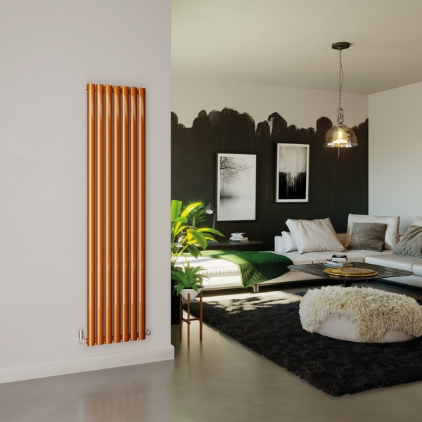 A vertical 7 column radiator in a vibrant copper finish situated on a plain white wall. Behind the wall to teh right is a dark sitting room with a large white corner sofa covered in white and grey square pillows and big deep green knitted throw. 