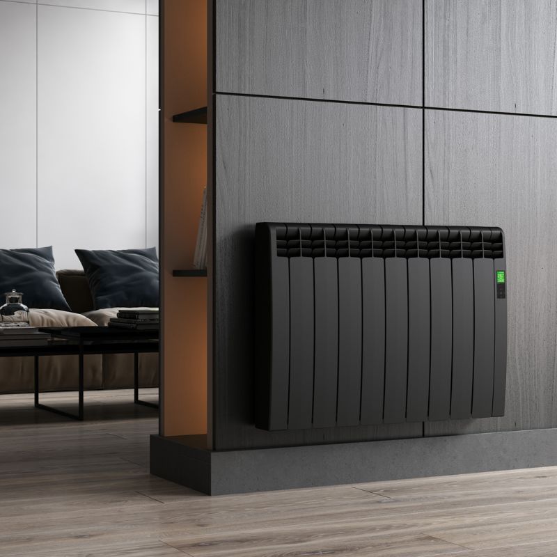 A black curved panel electric radiator mounted on a dark wooden wall. This is in a living room where there is a black table a large, light brown sofa with black cushions.