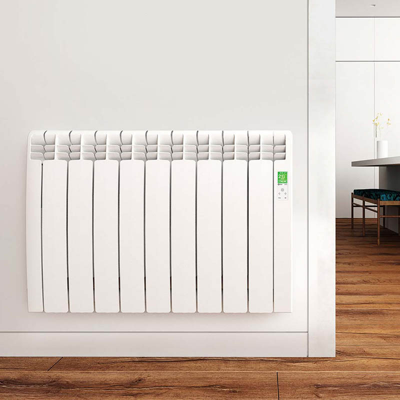 White curved panel electric radiator on a white wall. It is in a kitchen, their is warm wooden floor and wooden bench in the background.