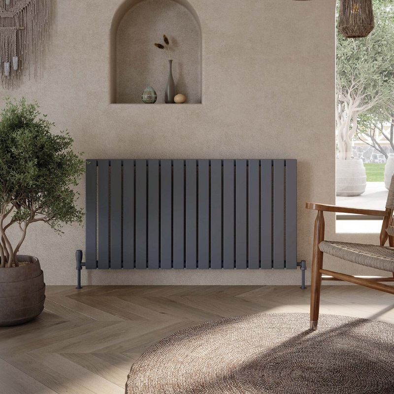 A dark grey horizontal radiator with 17, slim, horizontal rectangle panels. It is placed against a light beige, textured wall and on a light wood herringbone floor. 